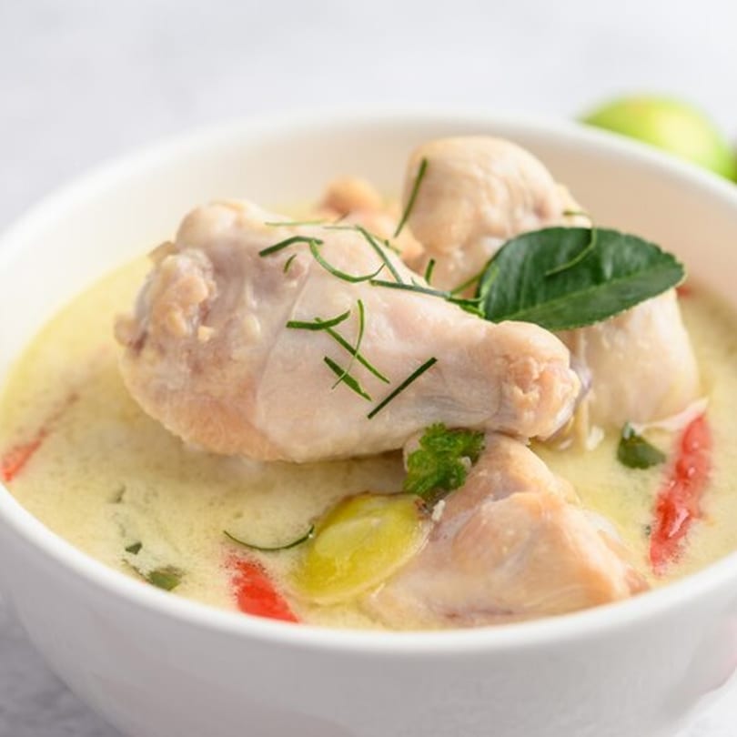 Chicken drumsticks in a creamy yellow sauce, garnished with herbs and red peppers in a white bowl.