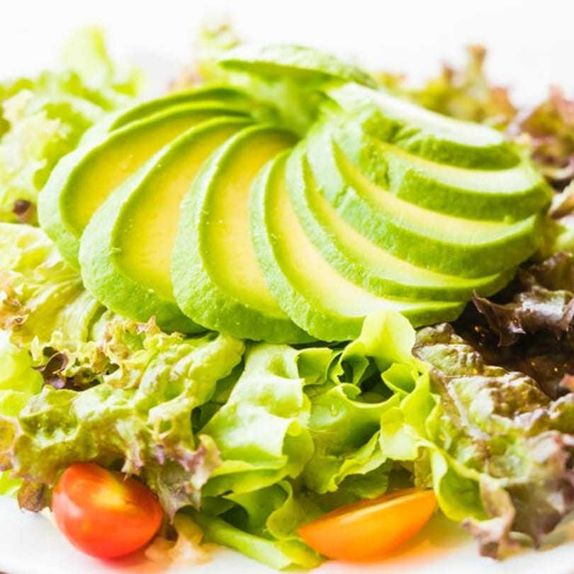 Fresh green and red lettuce salad topped with fanned avocado slices and cherry tomatoes.